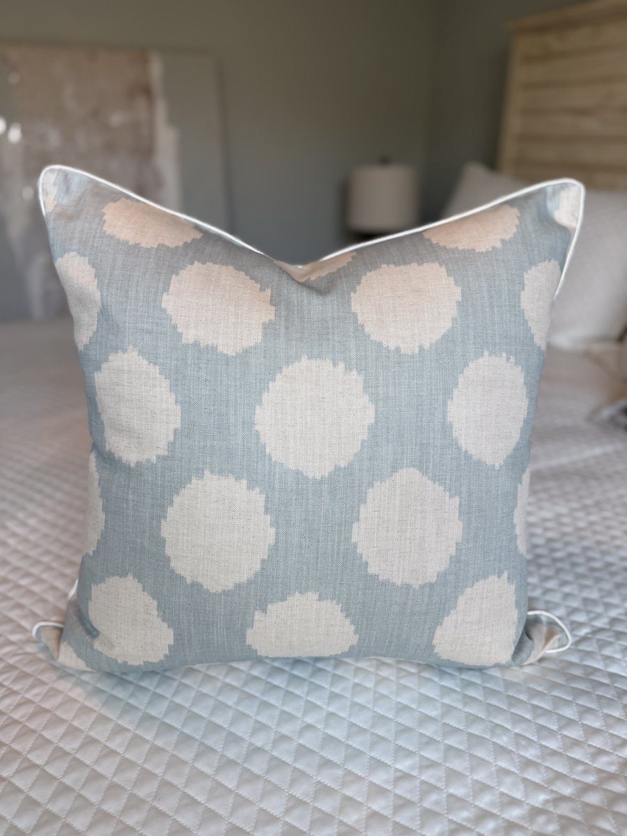 Duckie soft blue Andrew Martin ikat dot pillow front view styled on quilted bed