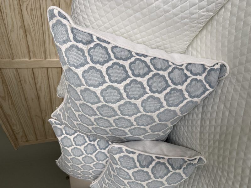 Genie blue quatrefoil pillows with white piping stacked on bed