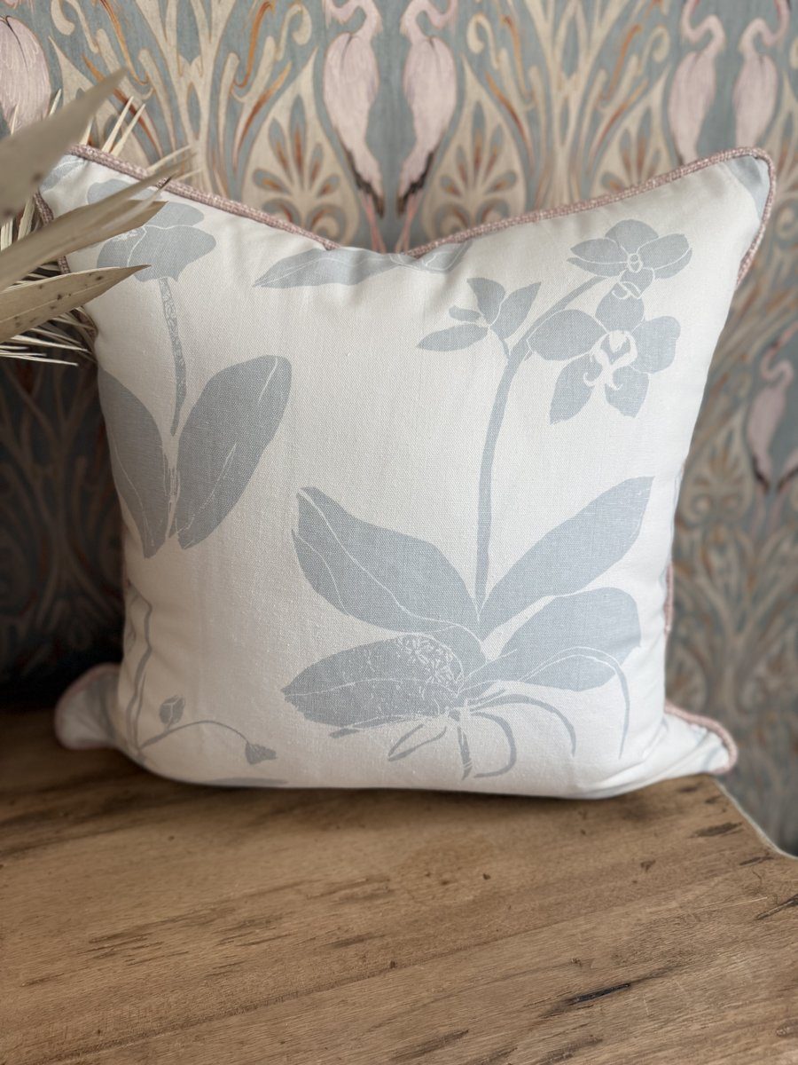 Orchids blue and white floral pillow styled against heron wallpaper on wood bench