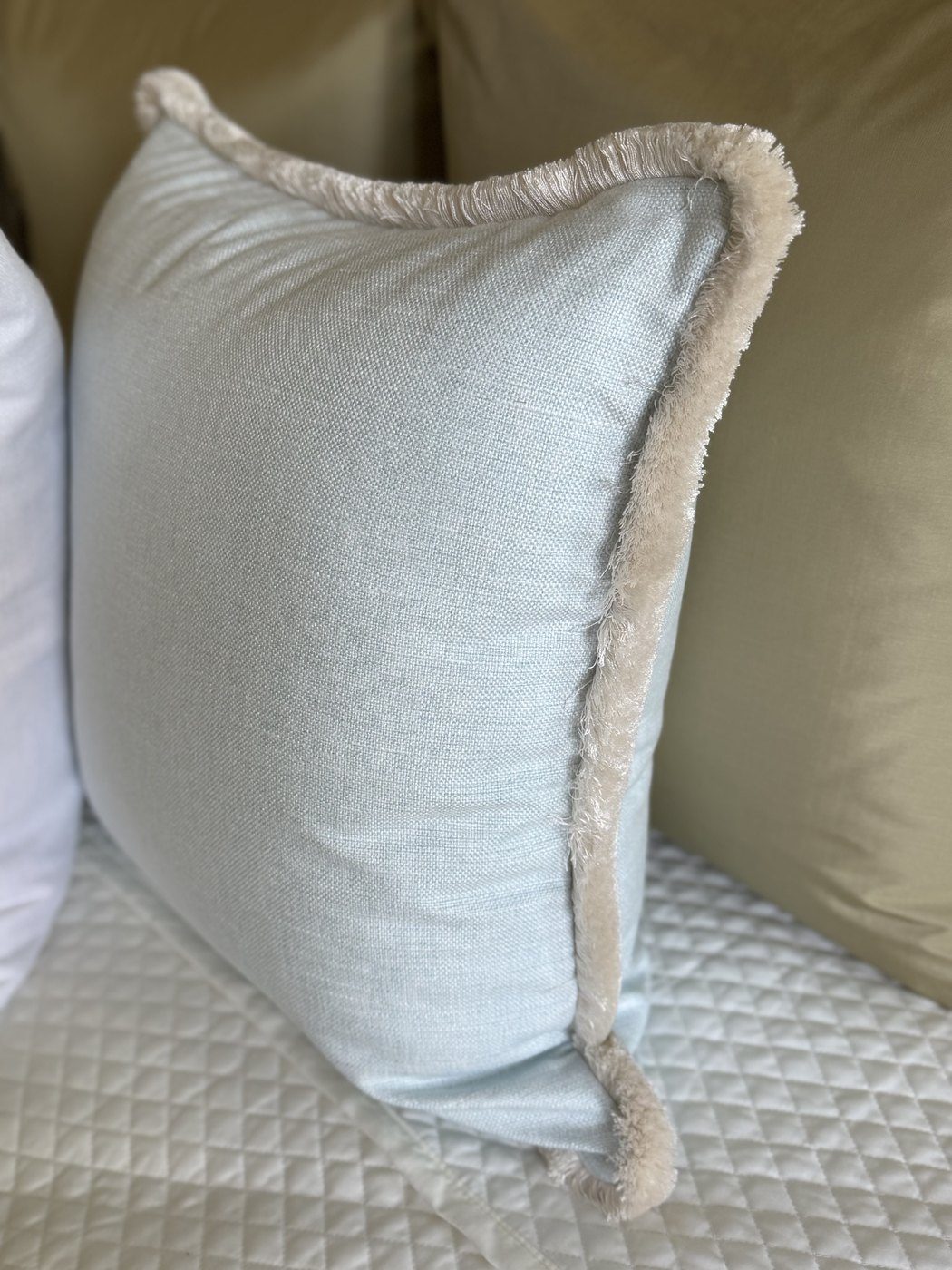 Simply Blue linen pillow side view with white brush fringe on bed